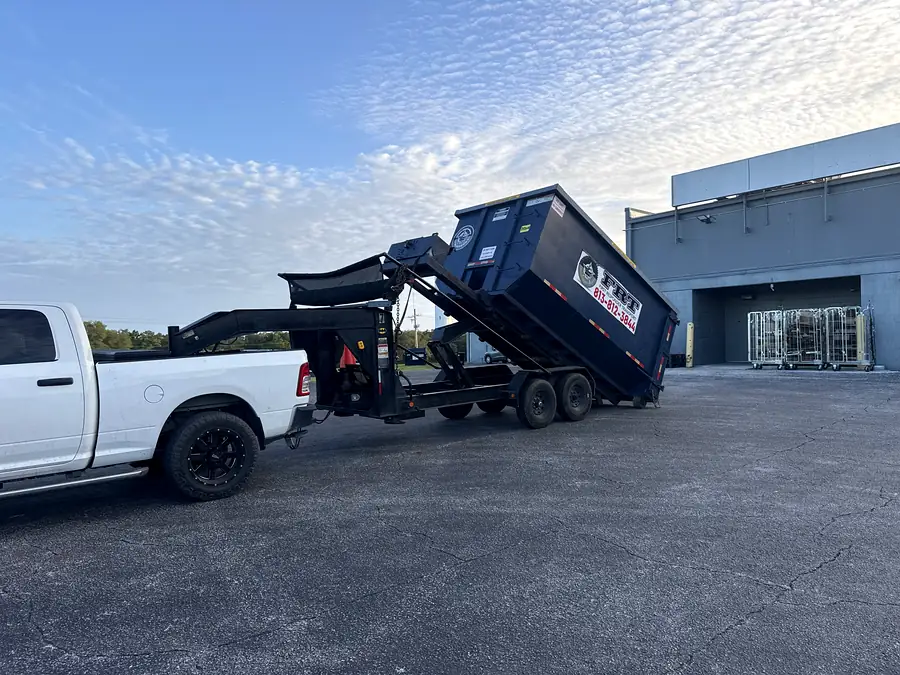 A dumpster being set down off the gooseneck trailer at a commercial site