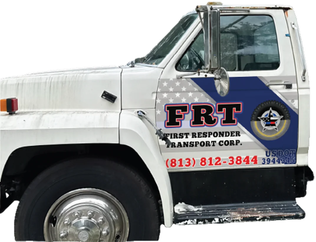 Driver's side of the FRT flatbed truck in navy and flag livery — the FRT badge, First Responder Transport Corp., (813) 812-3844 and USDOT 3944345 on the door.