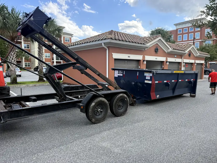 A roll-off dumpster and trailer outside an apartment building