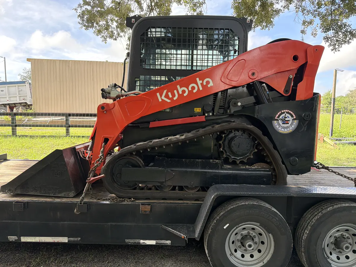 The tracked Kubota skid steer with the FRT badge on its side panel, chained down on the flatbed trailer